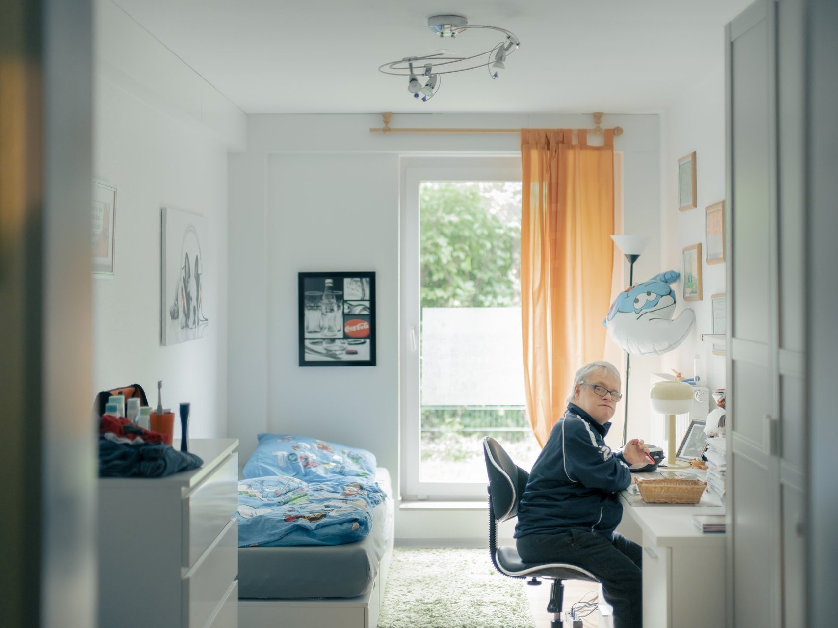 Ein junger Mann mit Behinderung sitzt in seinem lichtdurchfluteten Zimmer