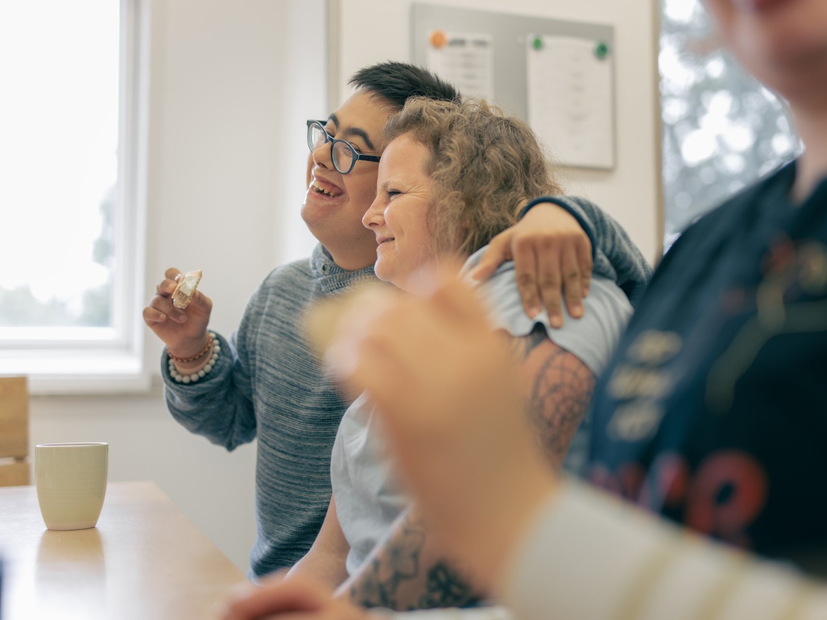 Pflegerin sitz mit einem Behinderten Jungen am Tisch und lachen zusammen