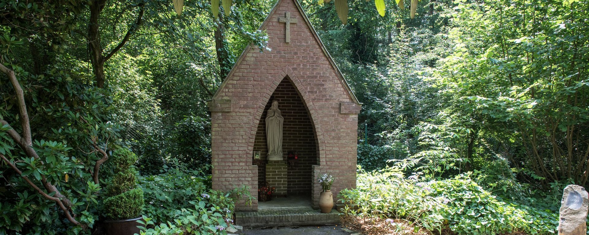 Madonnenstatue in einer kleinen Kapelle in einem Park umringt von vielen Pflanzen und Bäumen