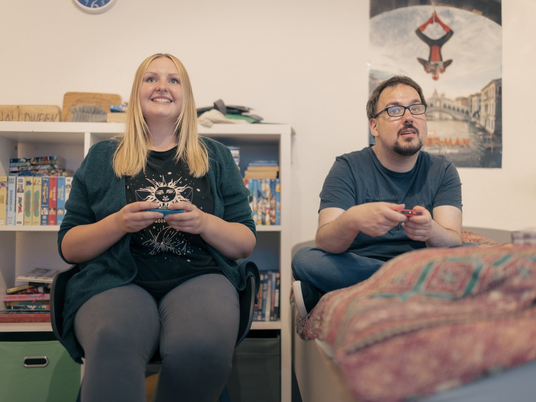 Eine junge Frau und ein Mann sitzen auf einem Bett und spielen mit einer Spielekonsole