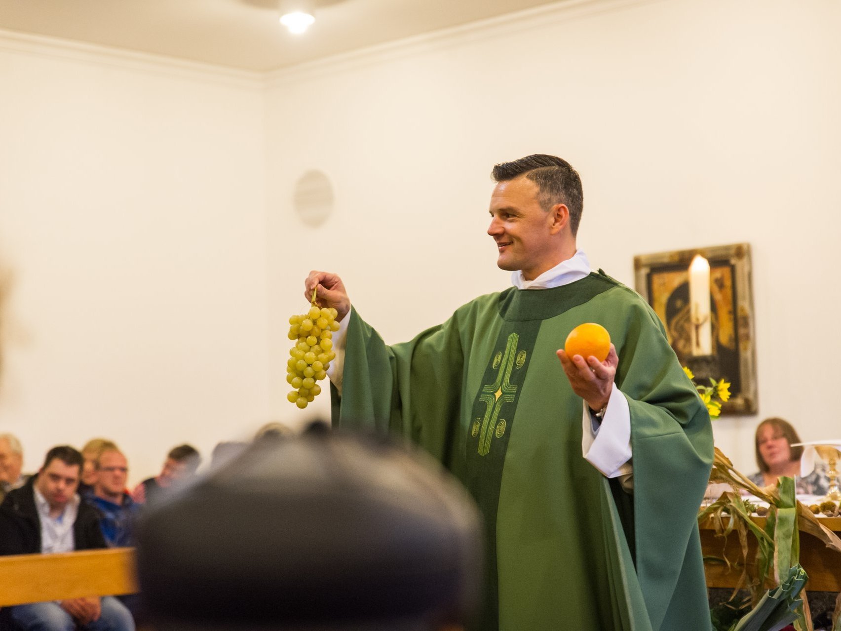 in der Kirche: Pater Jörg in der Kirche hält Weintrauben und eine Orange in der Hand