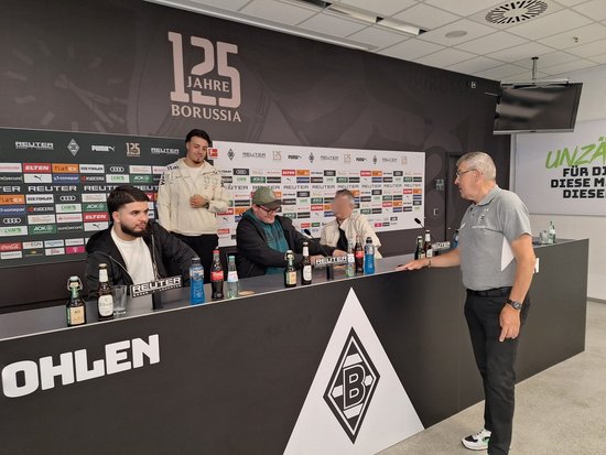 Im Bereich der Pressekonferenzen im Stadion von Borussia Mönchengladbach stehen fünf Männer vor einer Wand mit dem Schriftzug „125 JAHRE BORUSSIA“. Vier Männer sind am Tisch mit Mikrofonen und Getränken, einer steht rechts daneben und spricht. Das Vereinslogo ist auf dem Tisch sichtbar.