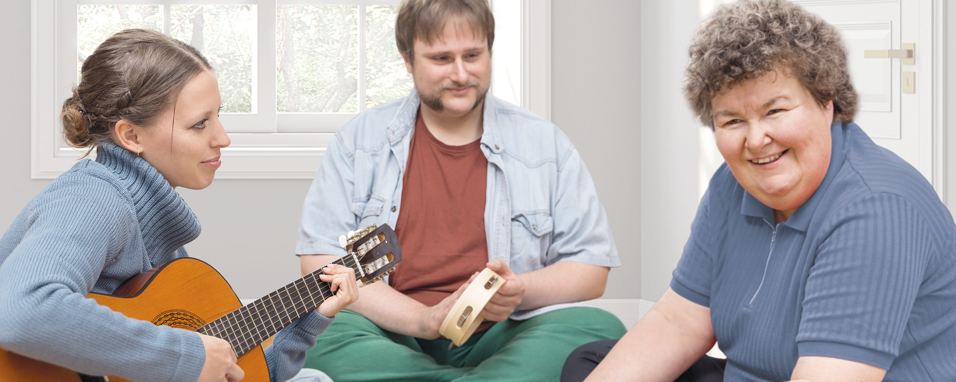 Eine junge Frau mit Gitarre begleitet eine Frau und einen Mann musikalisch
